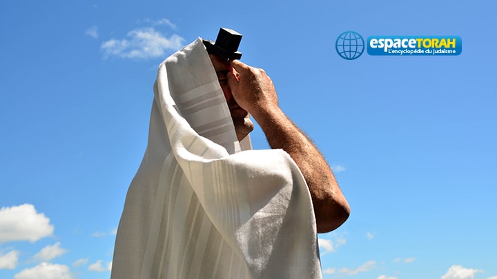 A Jewish man wearing Tallit and Tefillin read from the Torah book pray to God under a blue sky with sheep clouds. Photo by Rafael Ben-Ari/Chameleons Eye